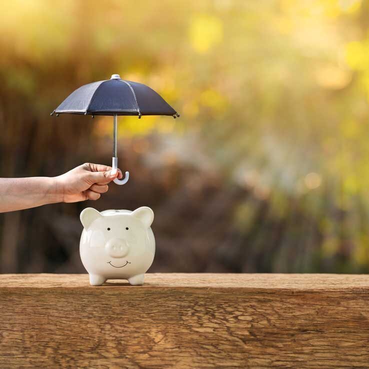 Kleines weißes Sparschwein auf Holzboden. Eine Hand hält einen kleinen Regenschirm über das Schwein